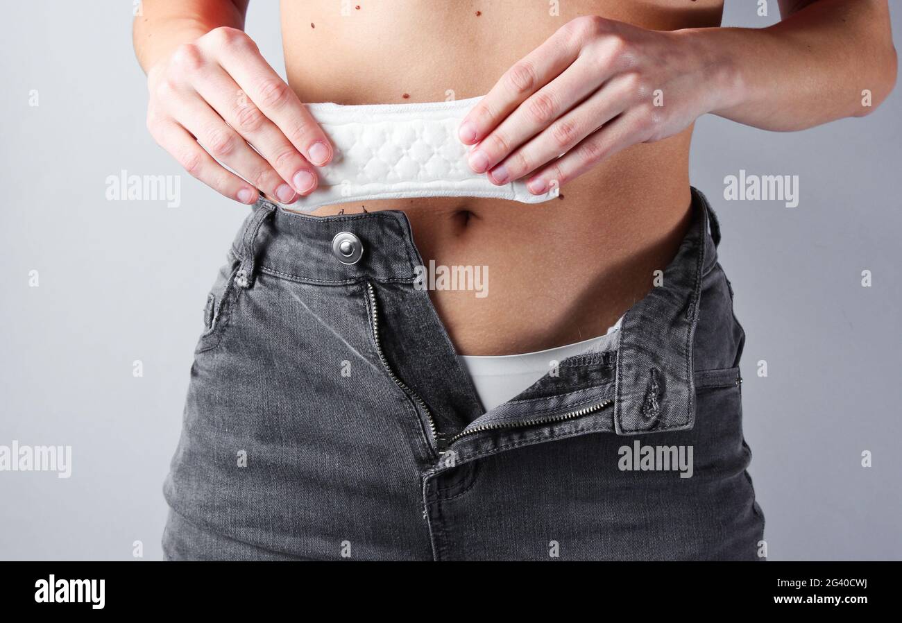 Woman with unbuttoned jeans holds pads in her hands on gray background