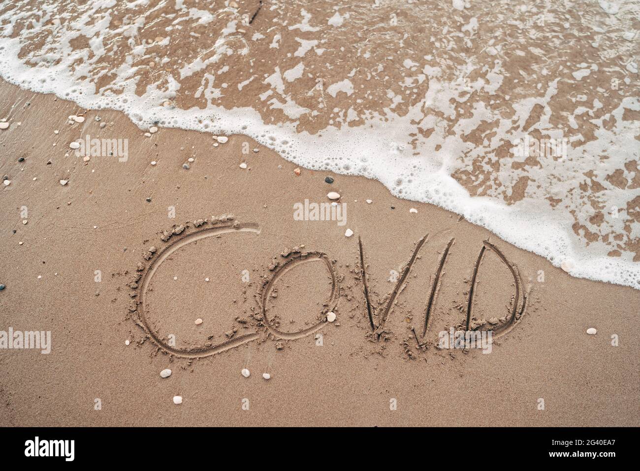 COVID inscription on the sand near the sea. The concept of canceling travel in 2020 and 2021 due to the Coronavirus pandemic in Stock Photo