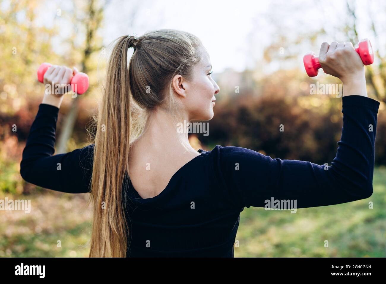 Beautiful woman working out outdoors. Sporty woman training with dumbbells, back view Stock Photo