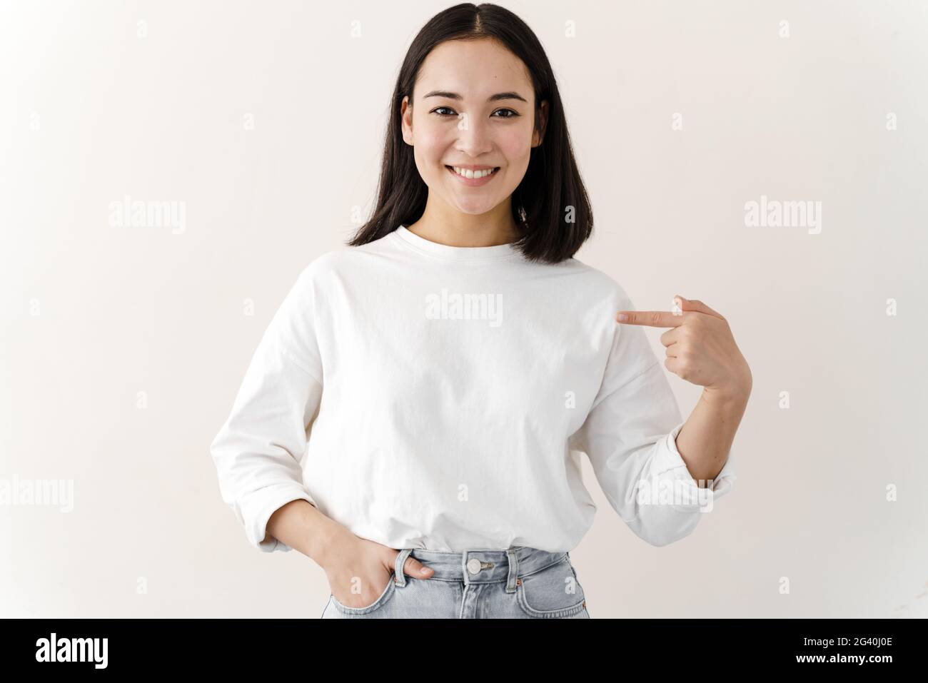 Clothing, design and advertising concept. Indoor shot of a positive young woman pointing to a copy space on her blank white t-shirt for your text or p Stock Photo