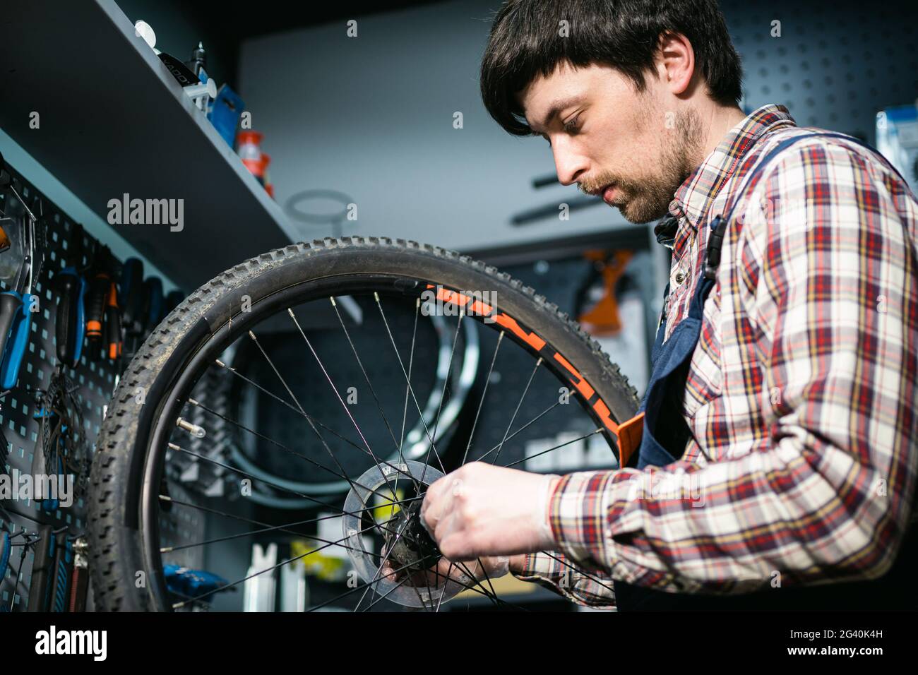 Young caucasian repairman repairing mountain bike wheel in bike shop workshop. Fixing bicycle. Caring for you wheels. man mechan Stock Photo
