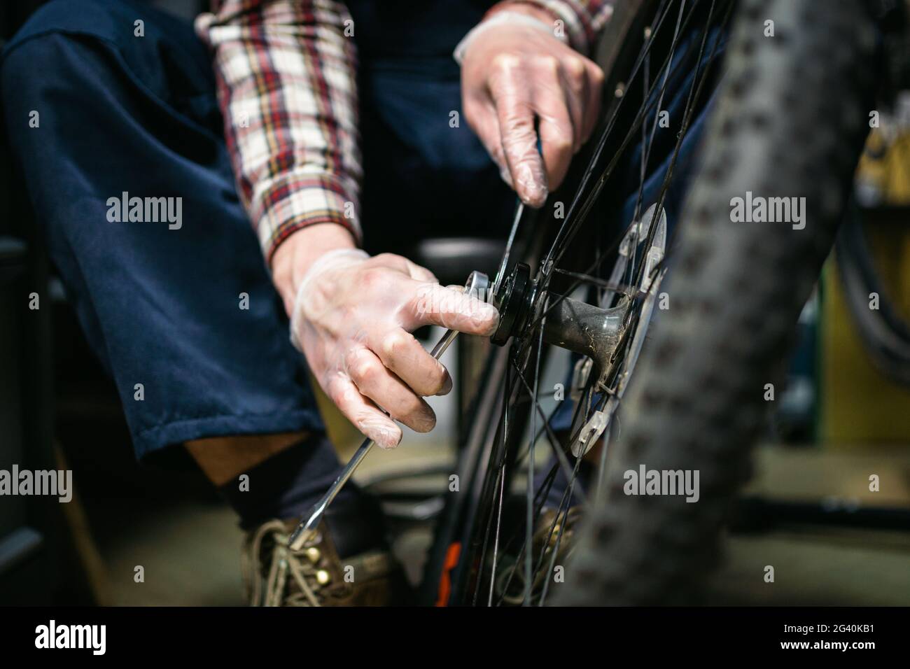 Male mechanic working in bicycle repair shop, mechanic repairing bike using special tool, wearing protective gloves. Young attra Stock Photo