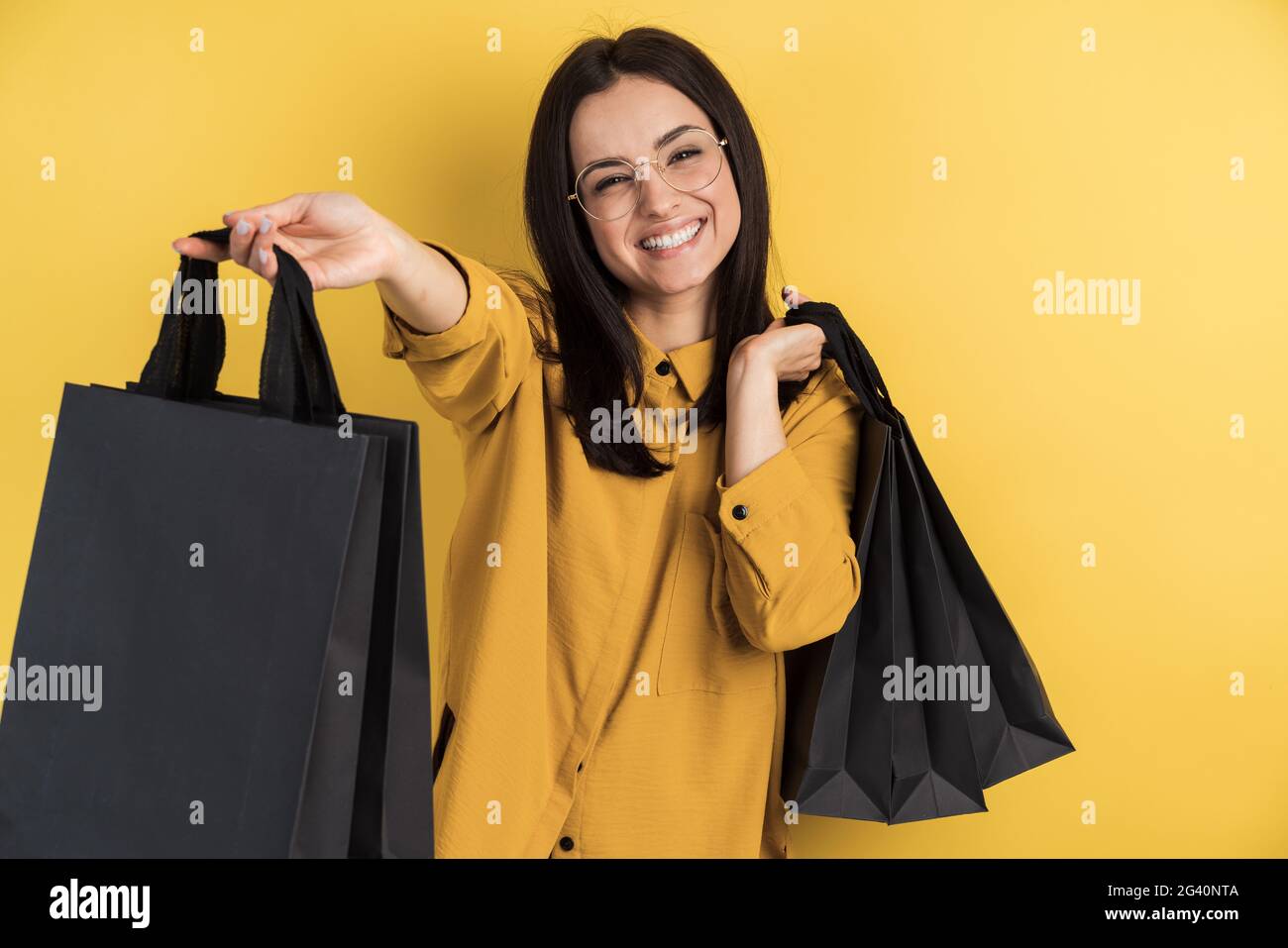 Happy stylish shopaholic woman in glasses holding shopping bags on orange studio background isolated. Young woman on a copy space Stock Photo