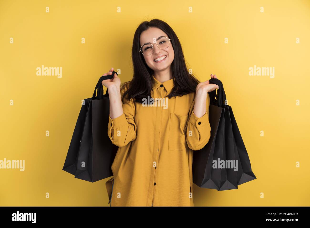 Attractive happy stylish shopaholic woman in glasses holding shopping bags on orange studio background, isolated. Stock Photo