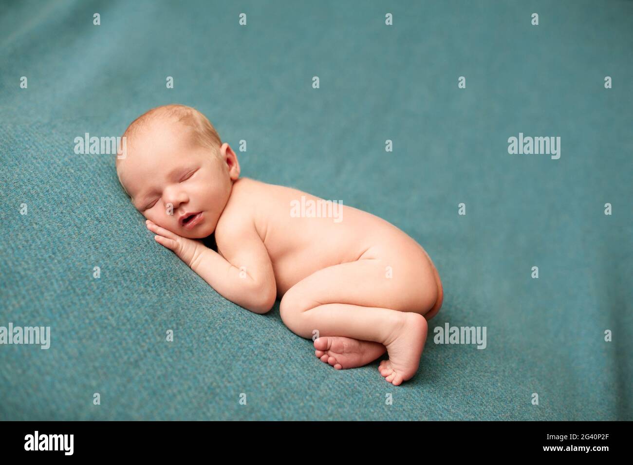Newborn baby boy sleeping at a newborn photoshoot with his hands under his cheeks Stock Photo