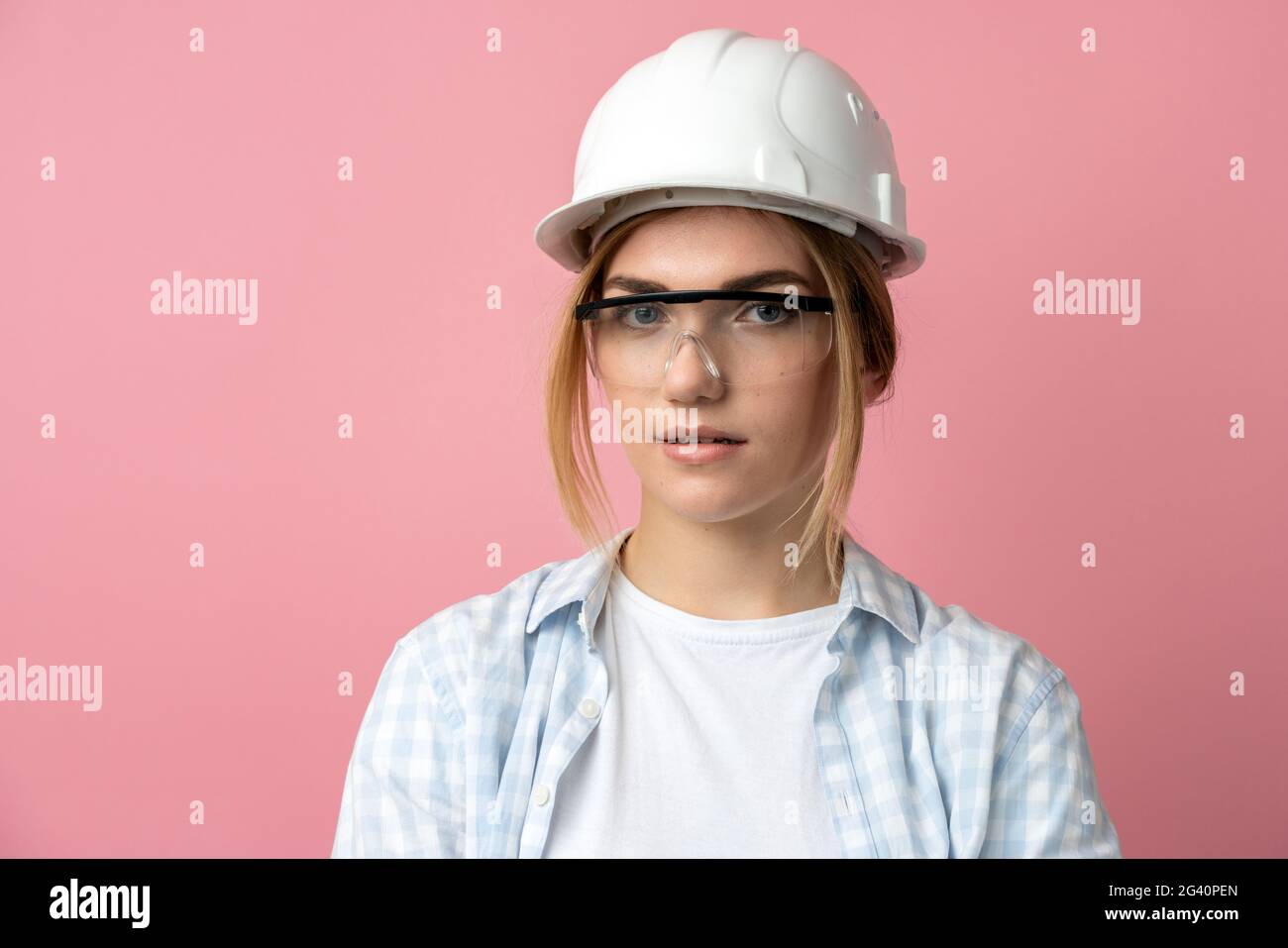 Young girl in a construction helmet on a background of a pink wall. Beautiful girl in