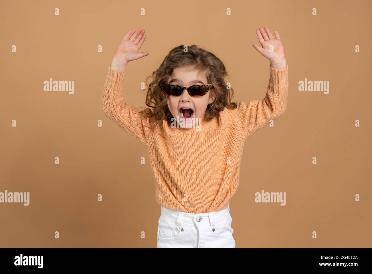 Playful, sweet little girl in sunglasses raised her hands as if to