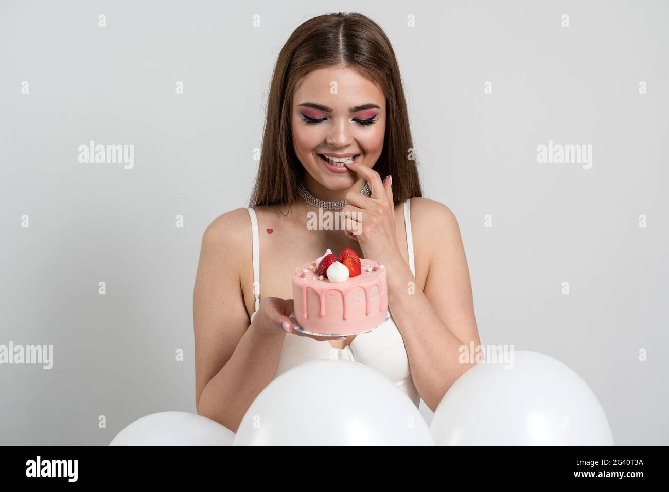 Sweet, attractive, well-groomed girl holds an appetizing cake, looks at it sincerely, wants to eat it. Beautiful, young woman on a white background, S Stock Photo