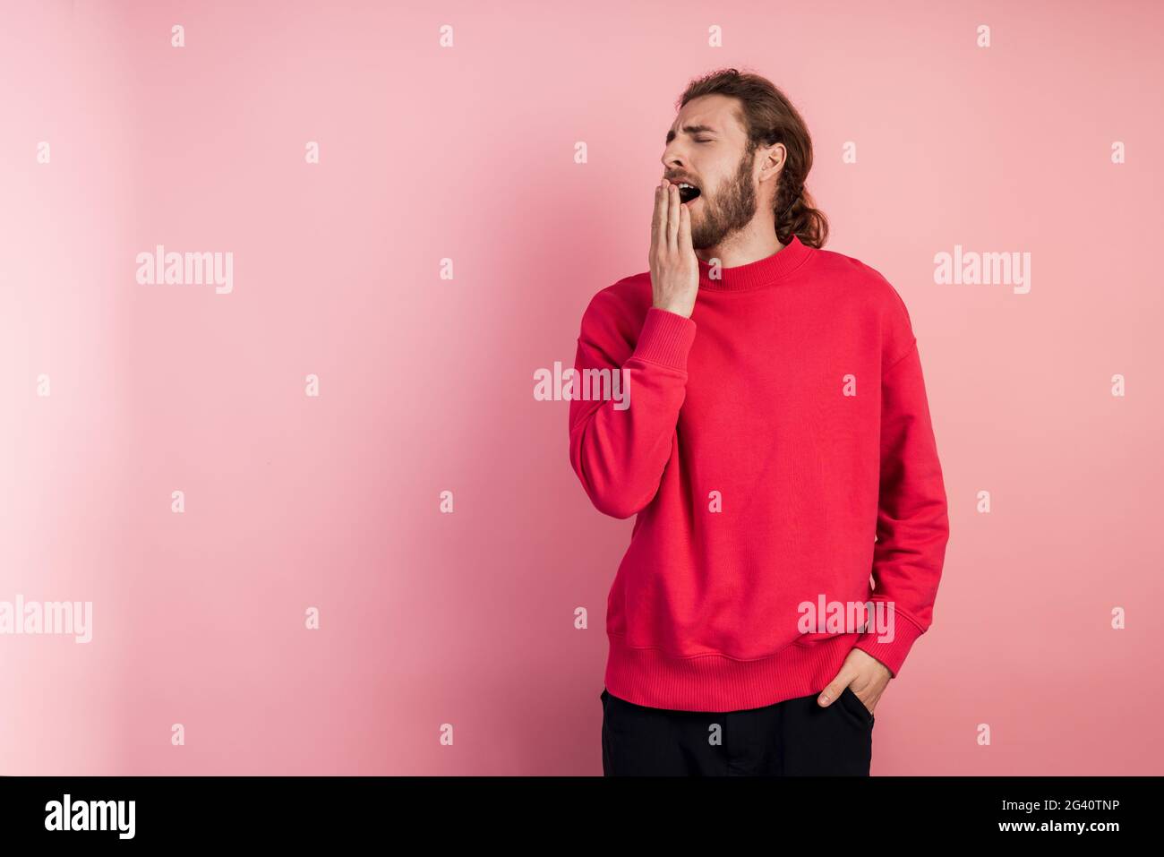 Young man wearing casual t-shirt standing on pink isolated background. Boring yawning tiredly covers his mouth with his hand. Anxiety and drowsiness. Stock Photo