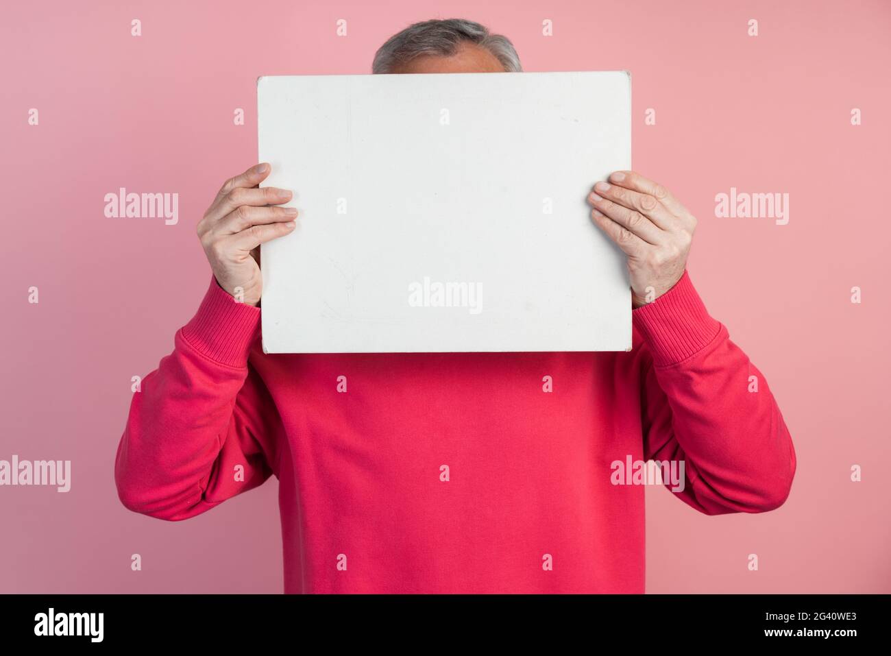 Man covers his face with a white sheet of paper. On a pink background copy space, place for text