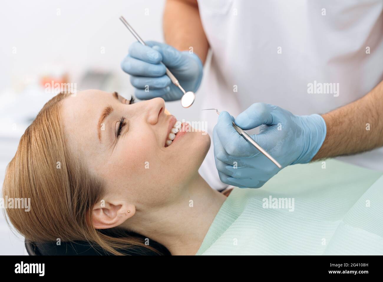 Attractive, charming woman sitting in a dental chair. The dentist examines the teeth with the help of dental instruments Stock Photo