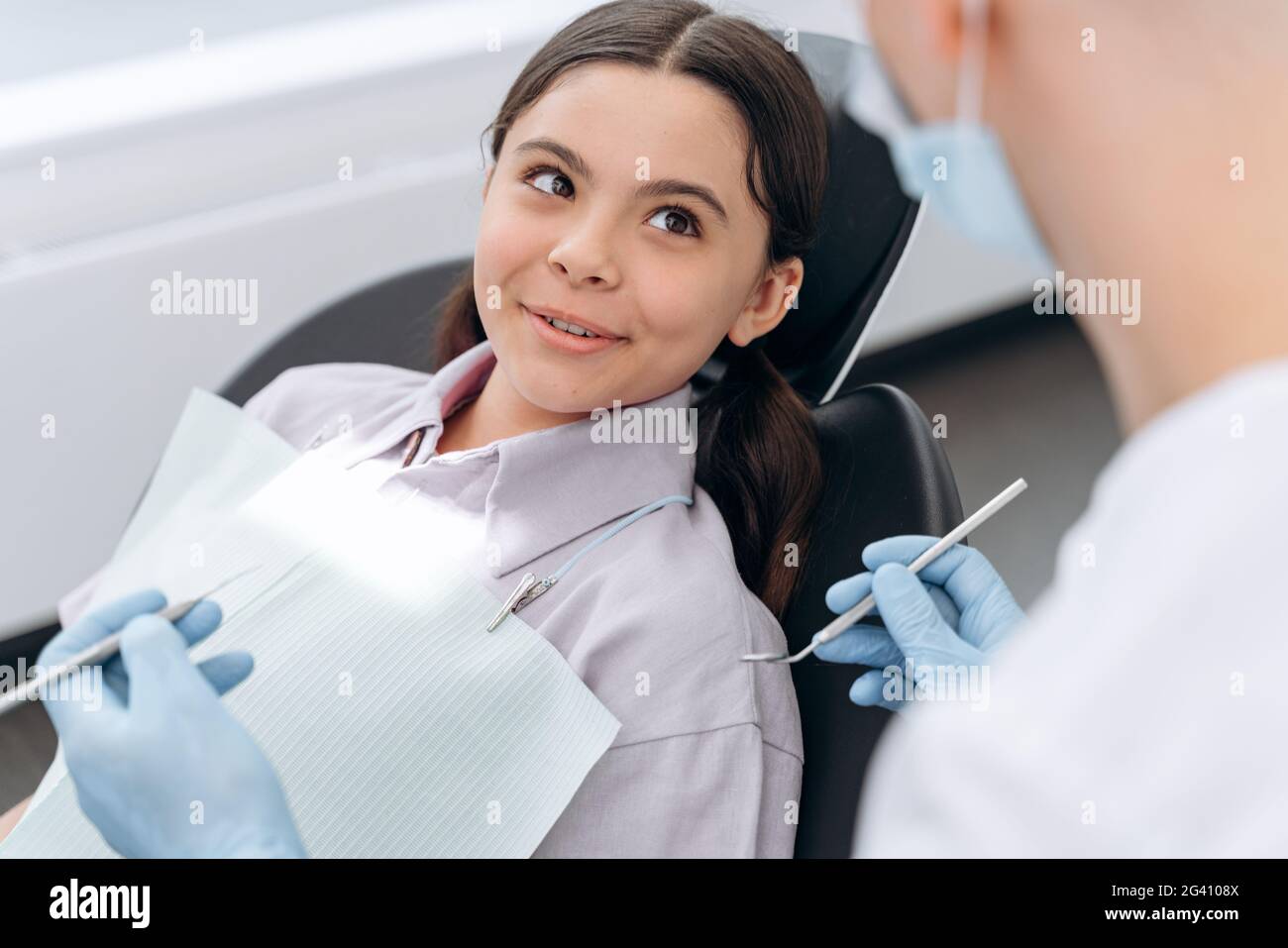 Positive little girl sitting in a dental chair. The dentist checks the teeth of a young patient Stock Photo