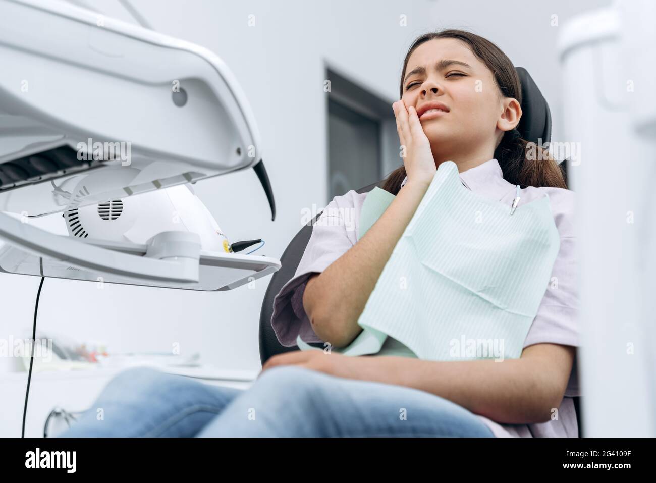 Girl in a dental chair holds her cheek. A cute girl has a toothache, bottom view Stock Photo