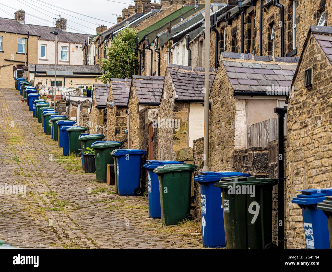 Sloping cobbled alley at rear of Victorian terraced houses in Skipton, UK, with lines of wheelie bins. Stock Photo