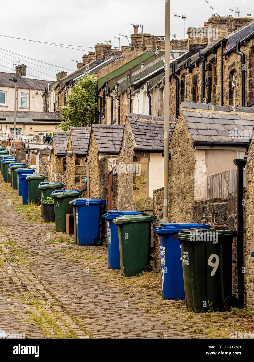 Sloping cobbled alley at rear of Victorian terraced houses in Skipton, UK, with lines of wheelie bins Stock Photo