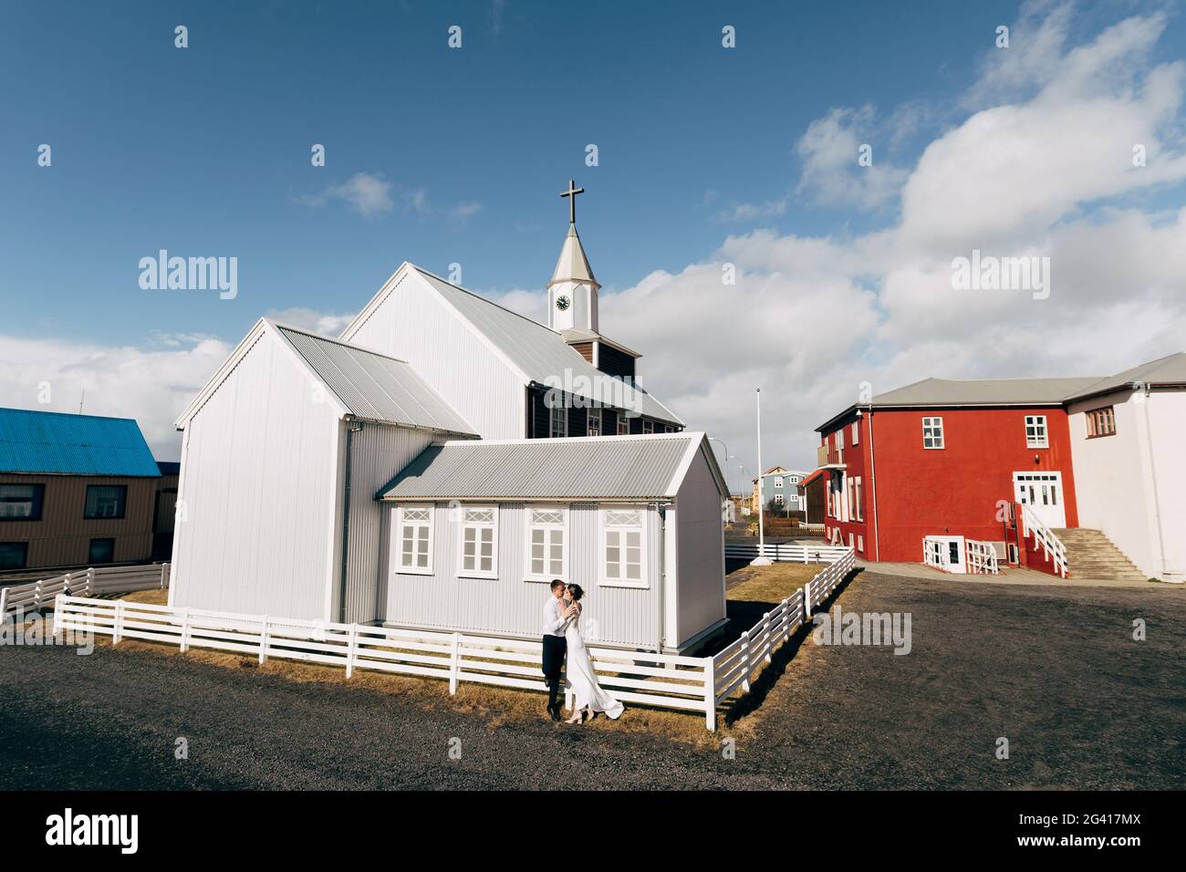 Destination Iceland wedding. Wedding couple near a wooden black church. The groom hugs the bride. Stock Photo