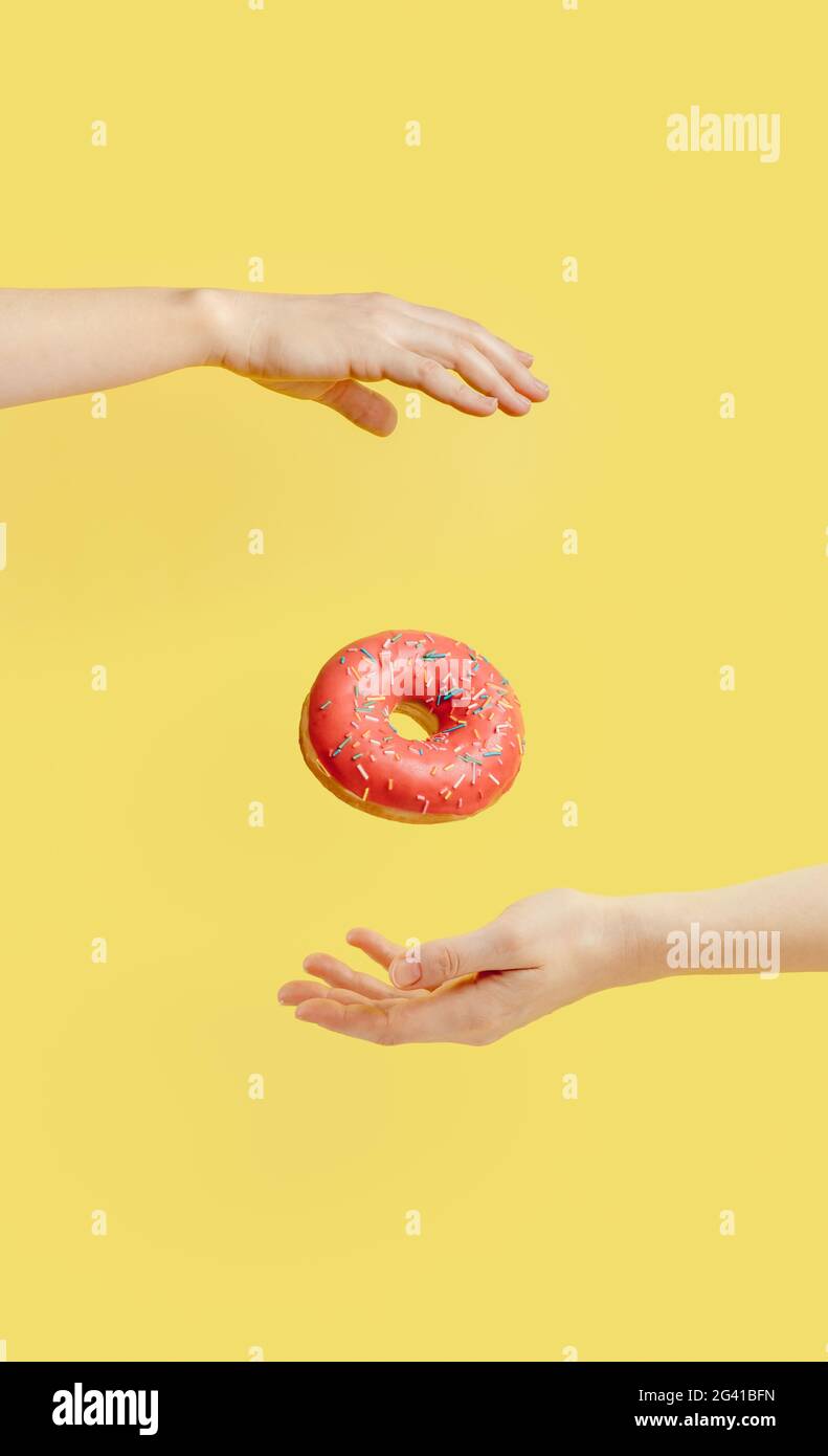 Donut falls between hands on yellow background Stock Photo