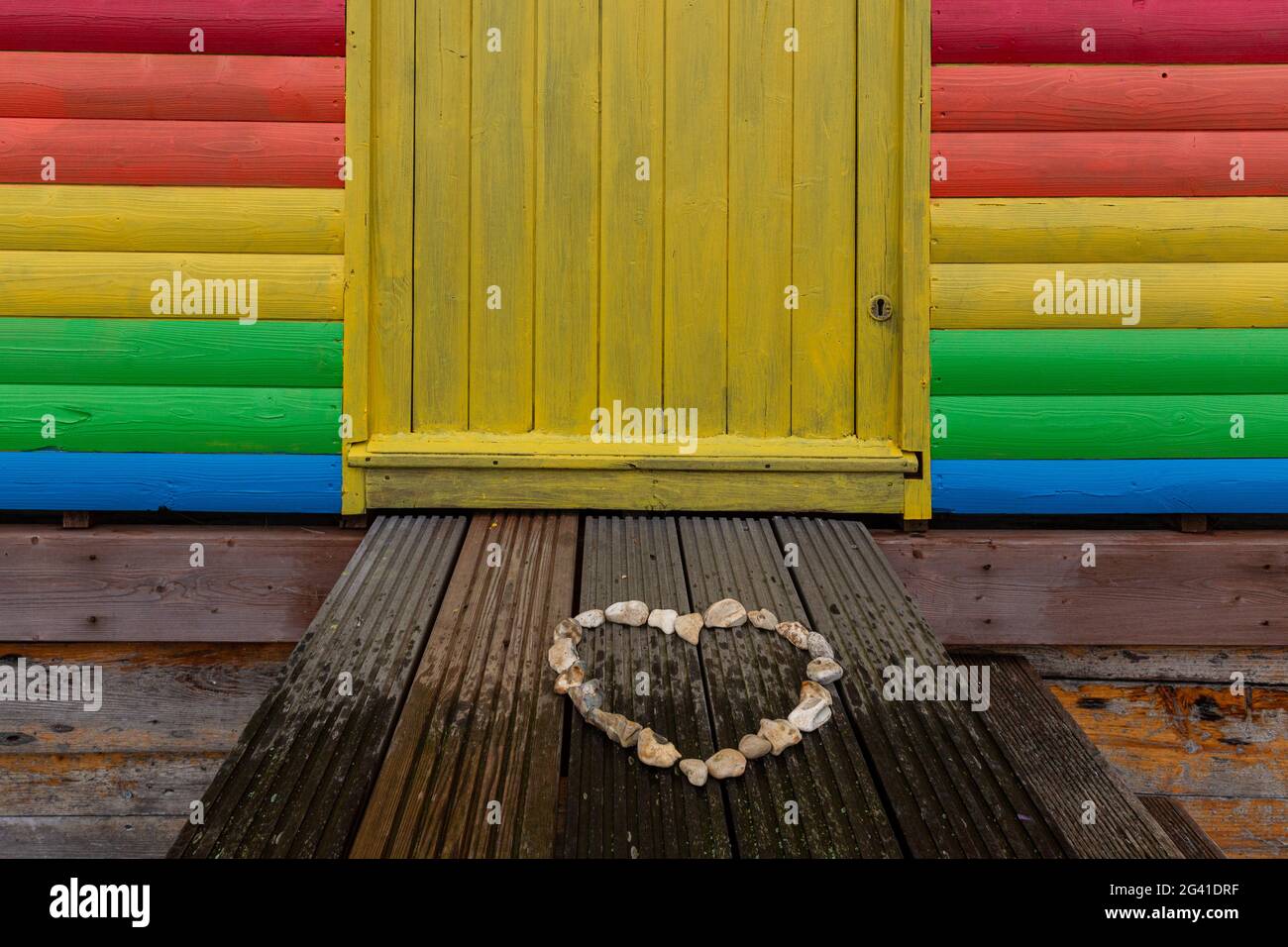 Whitstable, United Kingdom, June 18, 2021. A heart made of stones is seen in front of NHS colours wood shed at the beach  in Whitstable, a coastal touristic town in south-eastern England as vary poor rainy weather disturb holidaymakers as the holiday season begins. One of the strictest Coronavirus lockdowns in the world  is partially lifted as the United Kingdom managed to vaccinate a large part of the population and the number of Covid cases is low. People are able to socialize in limited numbers and are able to book holidays. Stock Photo