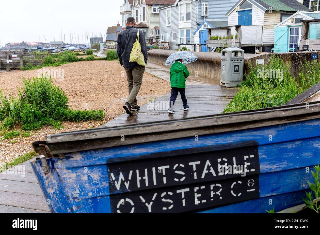Whitstable, United Kingdom, June 18, 2021. People walk at the beach  in Whitstable, a coastal touristic town in south-eastern England as vary poor rainy weather disturb holidaymakers as the holiday season begins. One of the strictest Coronavirus lockdowns in the world  is partially lifted as the United Kingdom managed to vaccinate a large part of the population and the number of Covid cases is low. People are able to socialize in limited numbers and are able to book holidays. Stock Photo