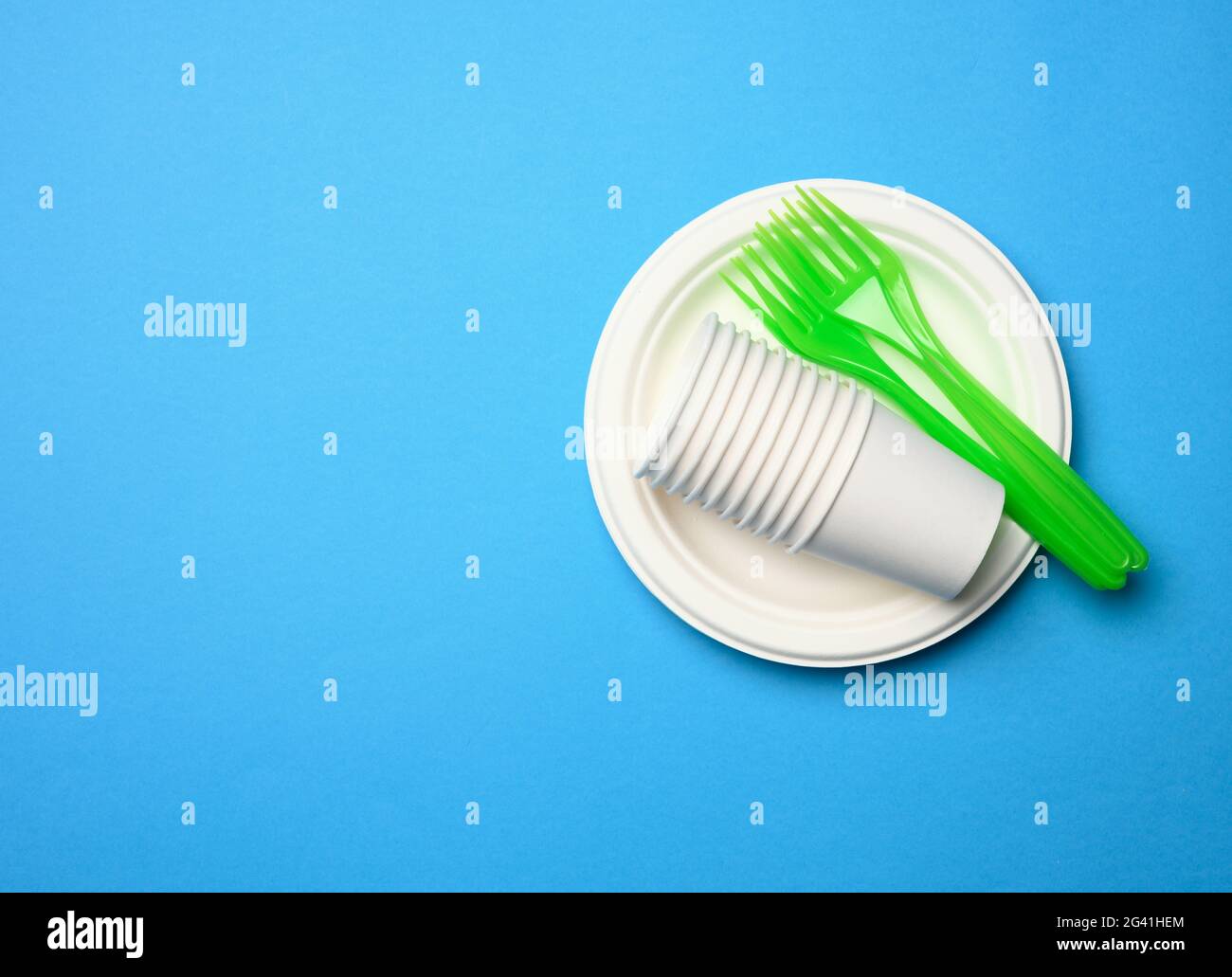 Green plastic forks and empty white paper disposable plates on a blue background, Stock Photo