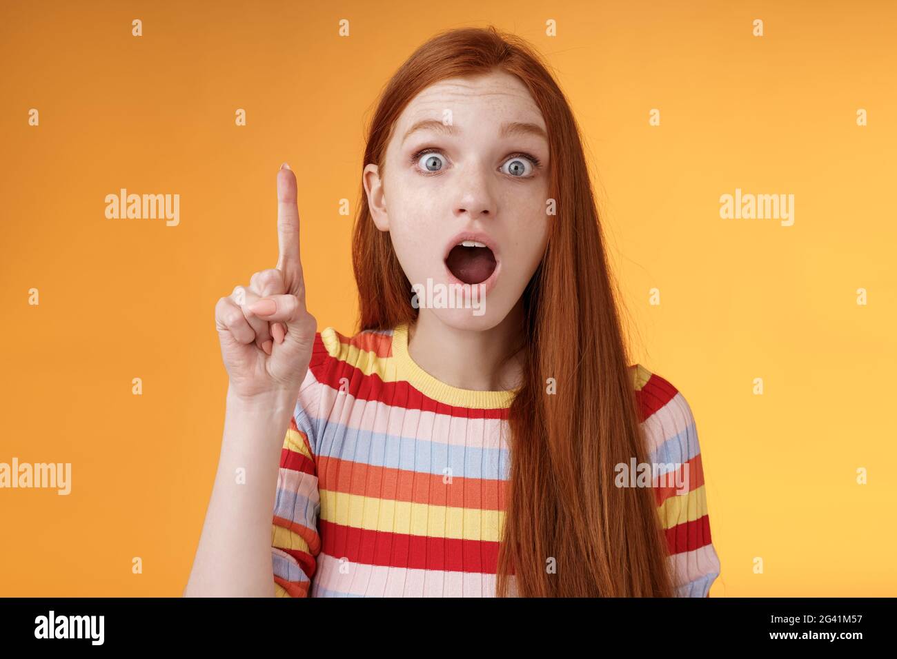 Got idea hurry listen. Excited young emotional redhead female coworker raising index finger eureka gesture open mouth wide eyes Stock Photo