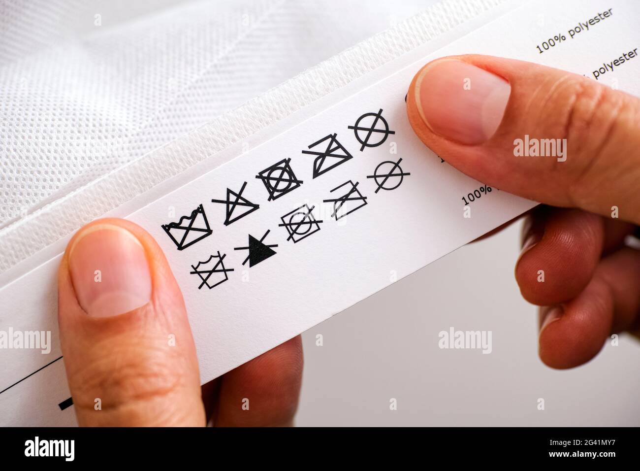 Woman's hands holding label with cleaning instructions of polyester thing - Do not wash; Do not bleach; Do not tumble dry; Do not dry flat; Do not iro Stock Photo