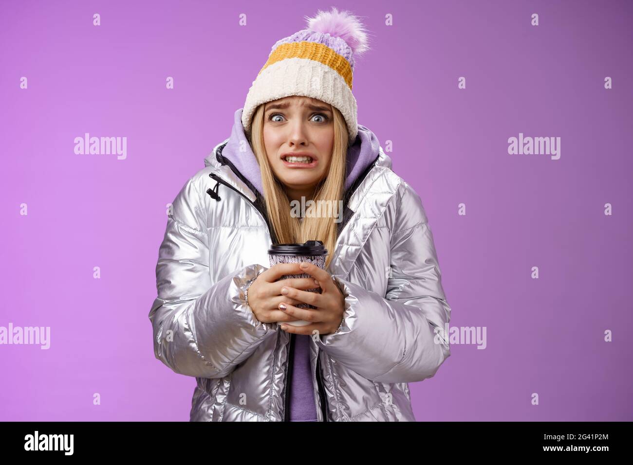Shaking uncomfortable displeased girl wearing stylish silver jacket hat trembling freezing cold warm hands holding take-away cof Stock Photo