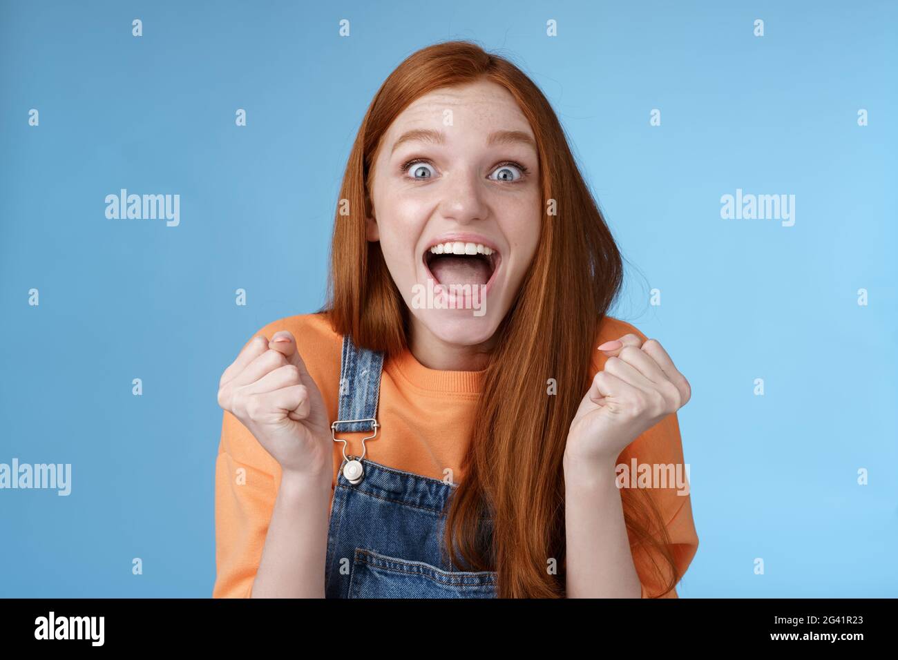 Excited happy overwhelmed cute ginger girl blue eyes yelling out loud rejoicing fantastic awesome news clench fists triumphing c Stock Photo