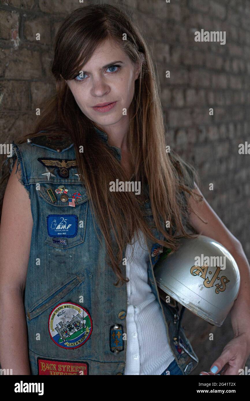 young woman with long hair wearing a rocker denim vest and holding a motorcycle  helmet Stock Photo - Alamy