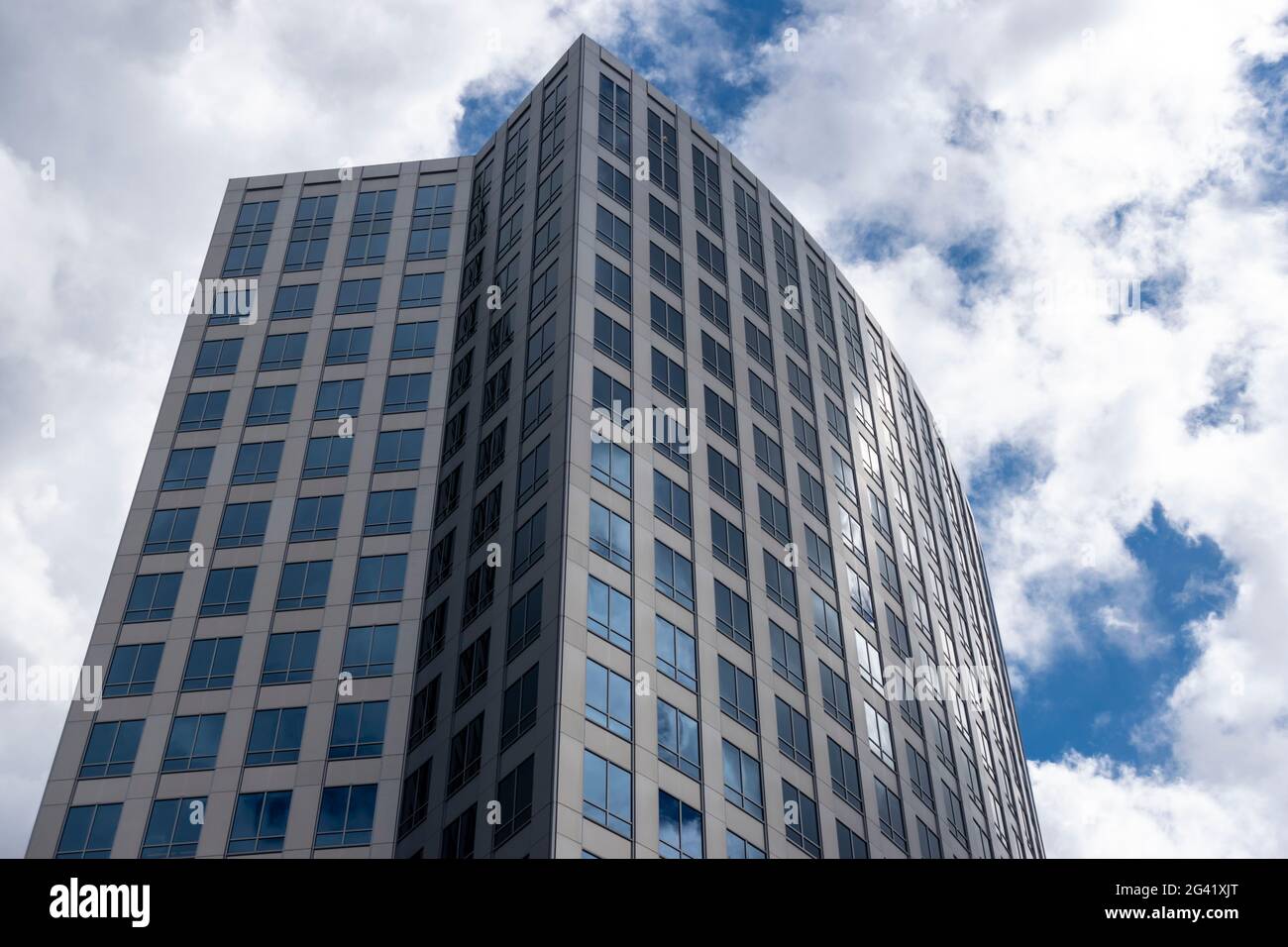 Angled view of a large, window covered building corner against a blue, cloud filled sky Stock Photo