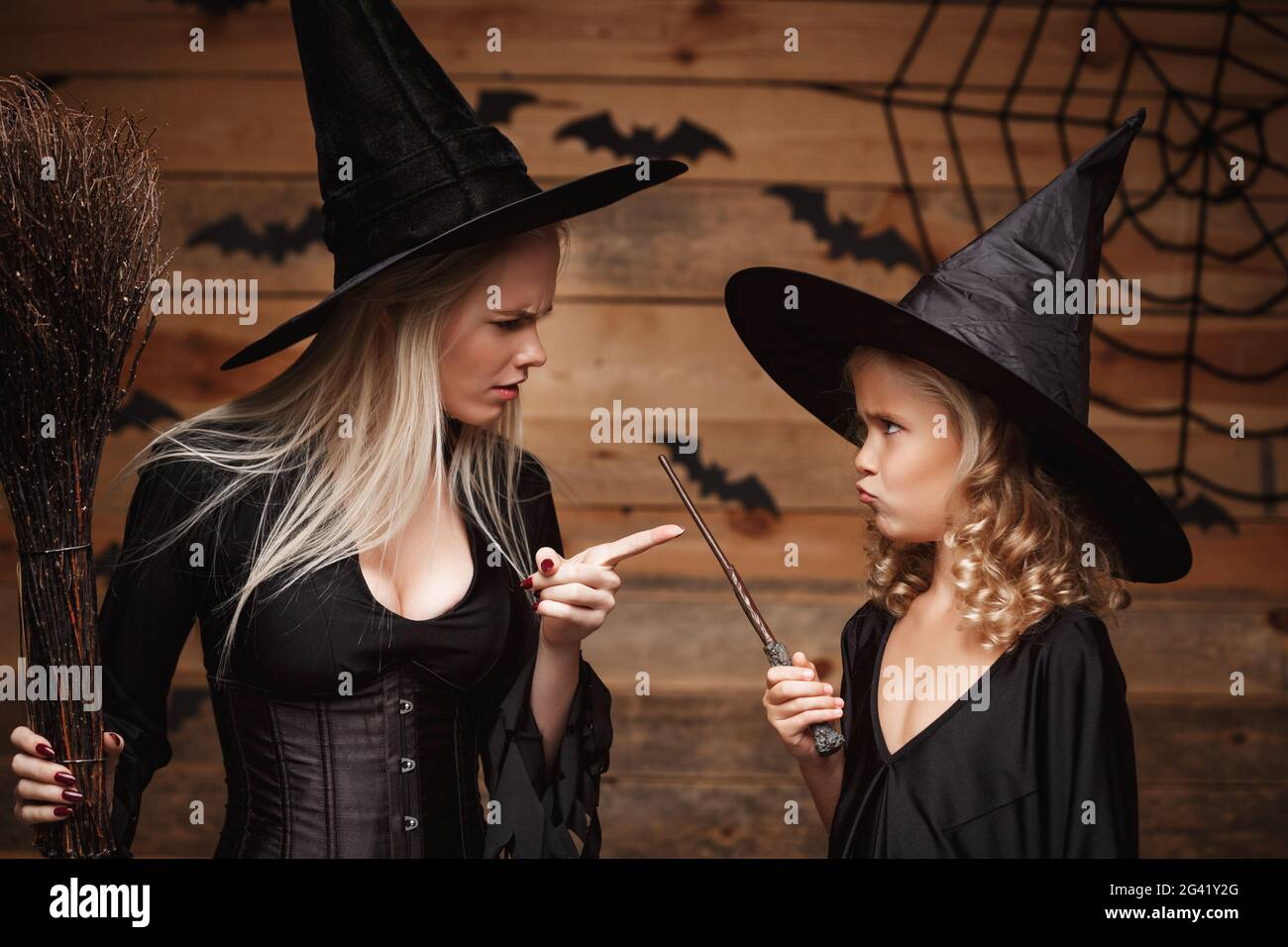 Halloween Concept - stressful witch mother teaching her daughter in witch costumes celebrating Halloween over bats and spider we Stock Photo