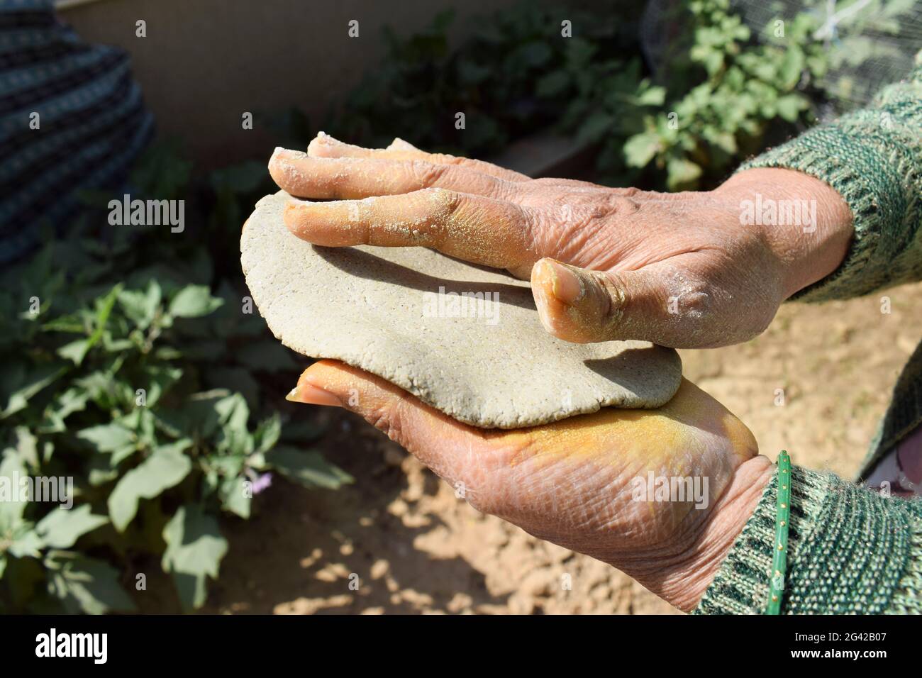 Woman making Indian or Pakistani flatbread made of pearl millet known as Bajre ki roti. Dough is flattened with hands to make round circle. Village st Stock Photo