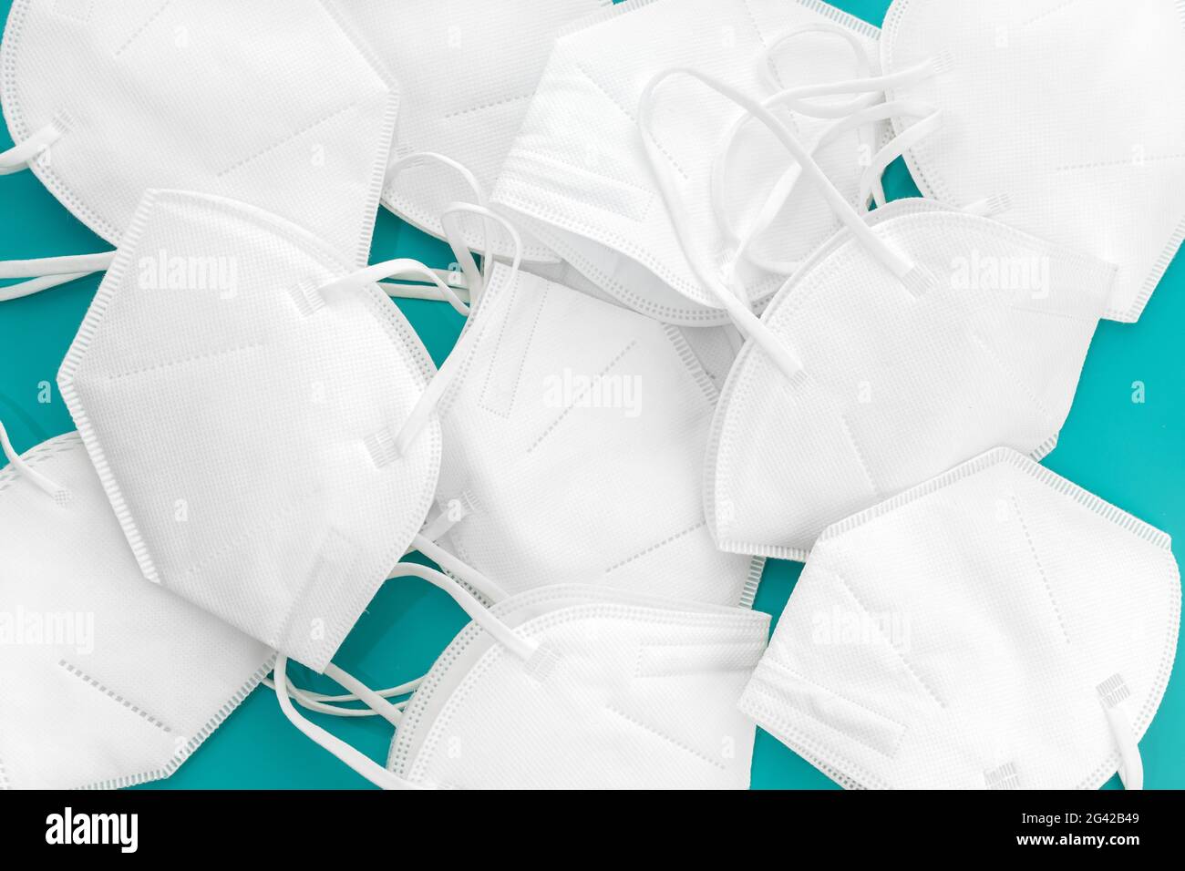 Group of used KN95 face mask on turquoise table. Coronavirus Covid-19 disposable masks wasting concept Stock Photo