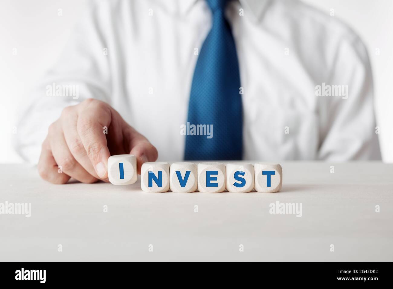 Businessman arranges wooden cubes with the word invest. Financial investment decision. Stock Photo