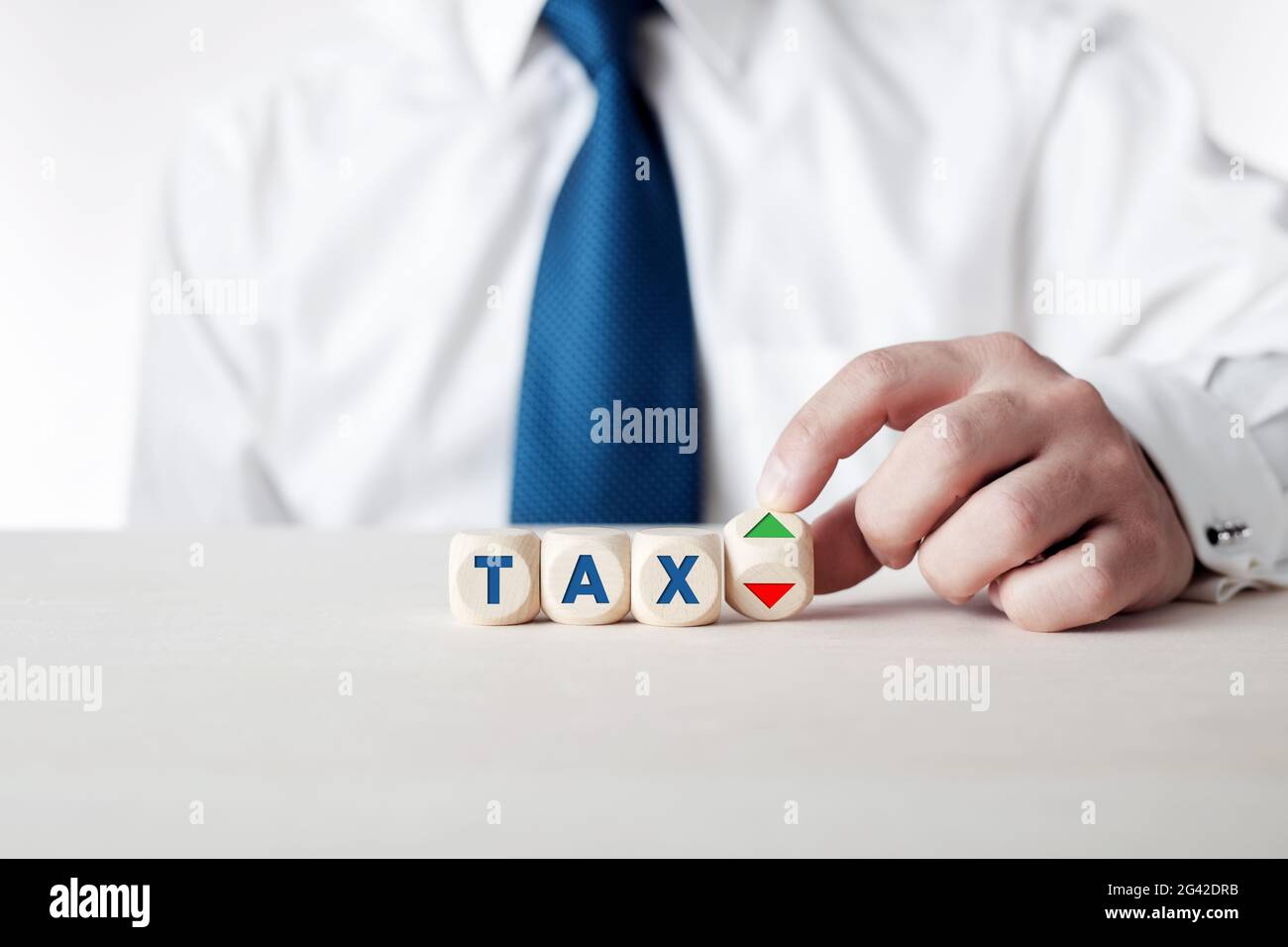 Businessman is turning a wooden cube with the arrows symbolizing the tax increase or reduction. Stock Photo