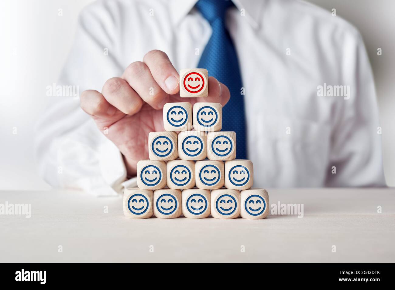 Businessman placing cube with happy smiling face symbol on top of tiered wooden cubes. Improve customer satisfaction concept. Stock Photo