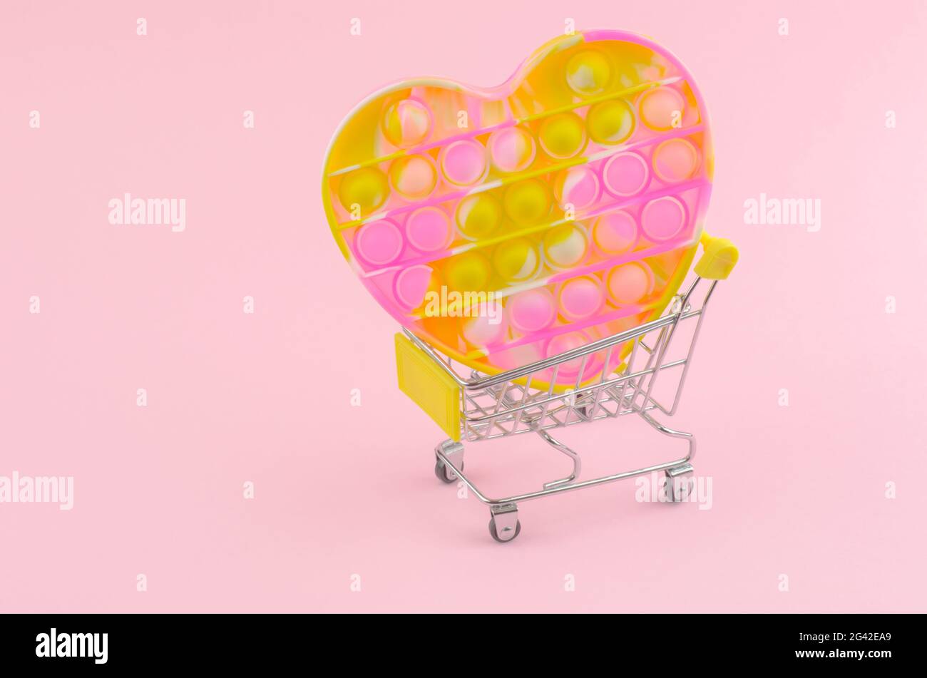 Pop it in the shape of a heart on a shopping trolley. Children's modern toy pop it fidget in female hands. Silicone toy for the development of fine mo Stock Photo