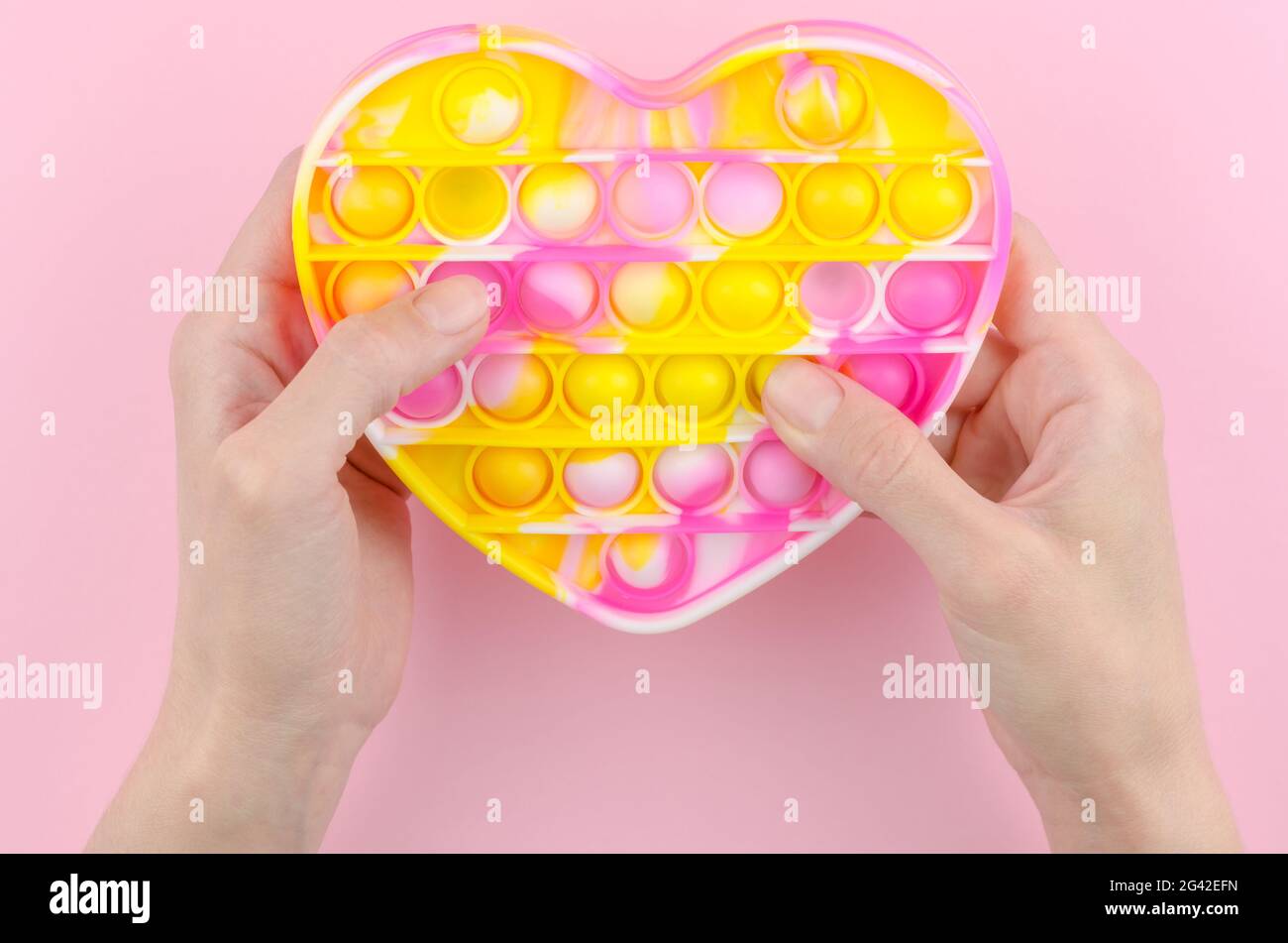 Pop it in the shape of a heart on a pink background. Children's modern toy pop it fidget in female hands. Silicone toy for the development of fine mot Stock Photo