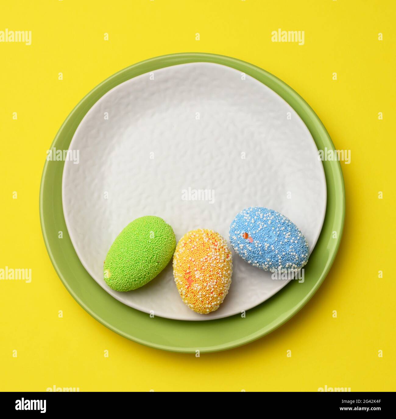 Decorative easter eggs in a round white ceramic plate on a yellow background Stock Photo