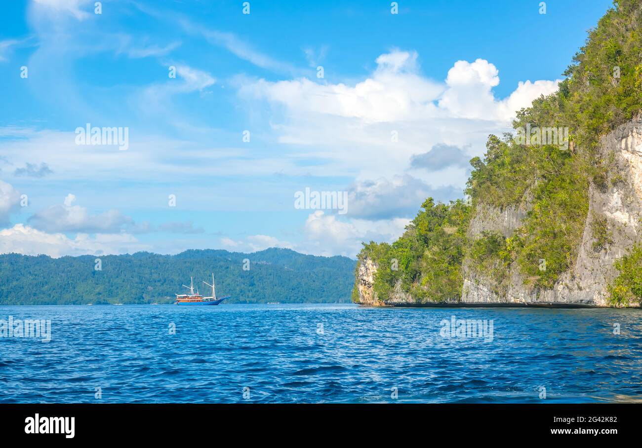 Coastal Rock With Rainforests and Yacht in the Distance Stock Photo