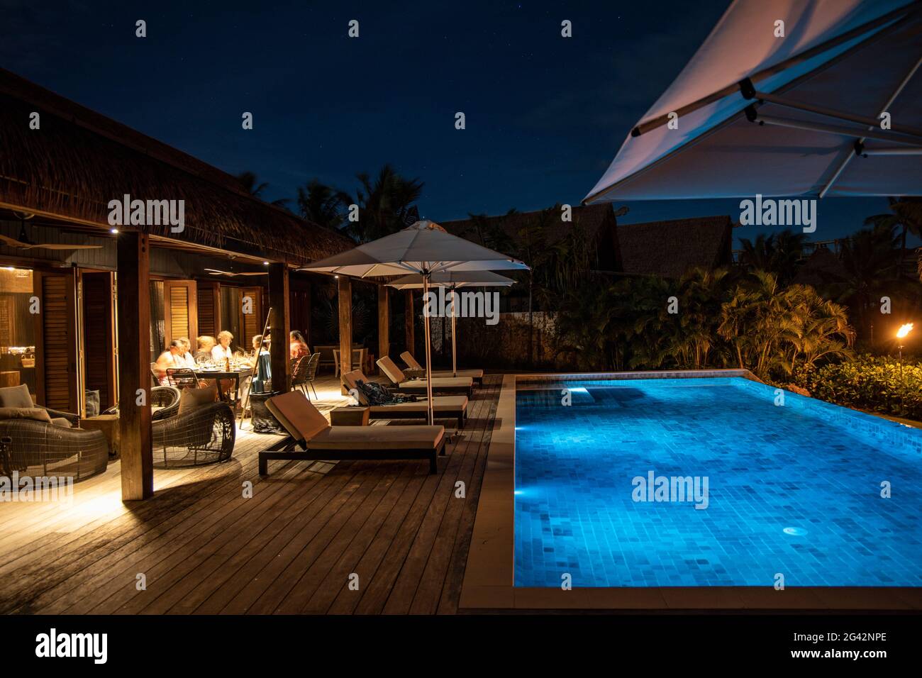 People enjoy dinner next to a private swimming pool of a Residence Villa accommodation at Six Senses Fiji Resort at night, Malolo Island, Mamanuca Gro Stock Photo