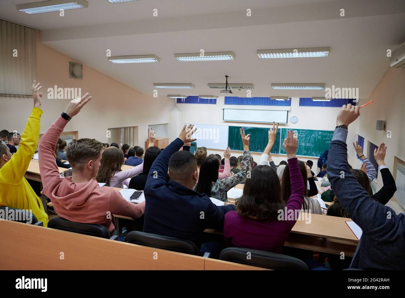 Raised hands and arms of large group of people in class room Stock Photo