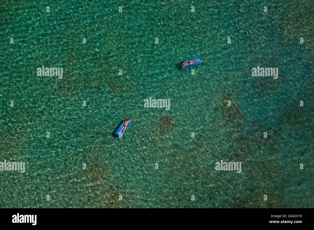 Two women floating on rubber floats in a clear blue ocean. Shot from the air. British Virgin Islands. Stock Photo