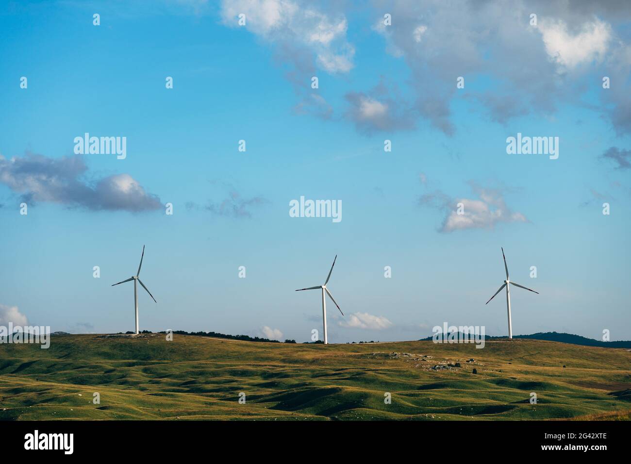 Three high wind turbines in the field against the blue sky. Stock Photo