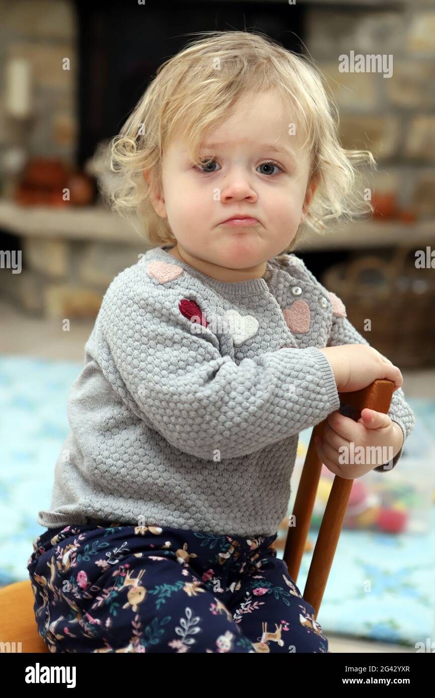 Little girl sitting on a wooden child chair in living room and makes a snort Stock Photo