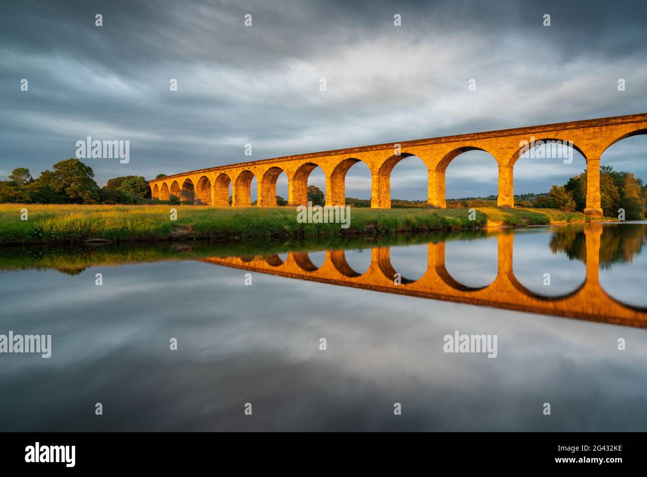 A burst of late evening sunlight turns the arches of Arthington Viaduct golden on a warm summer evening with perfect reflections in the River Wharfe. Stock Photo