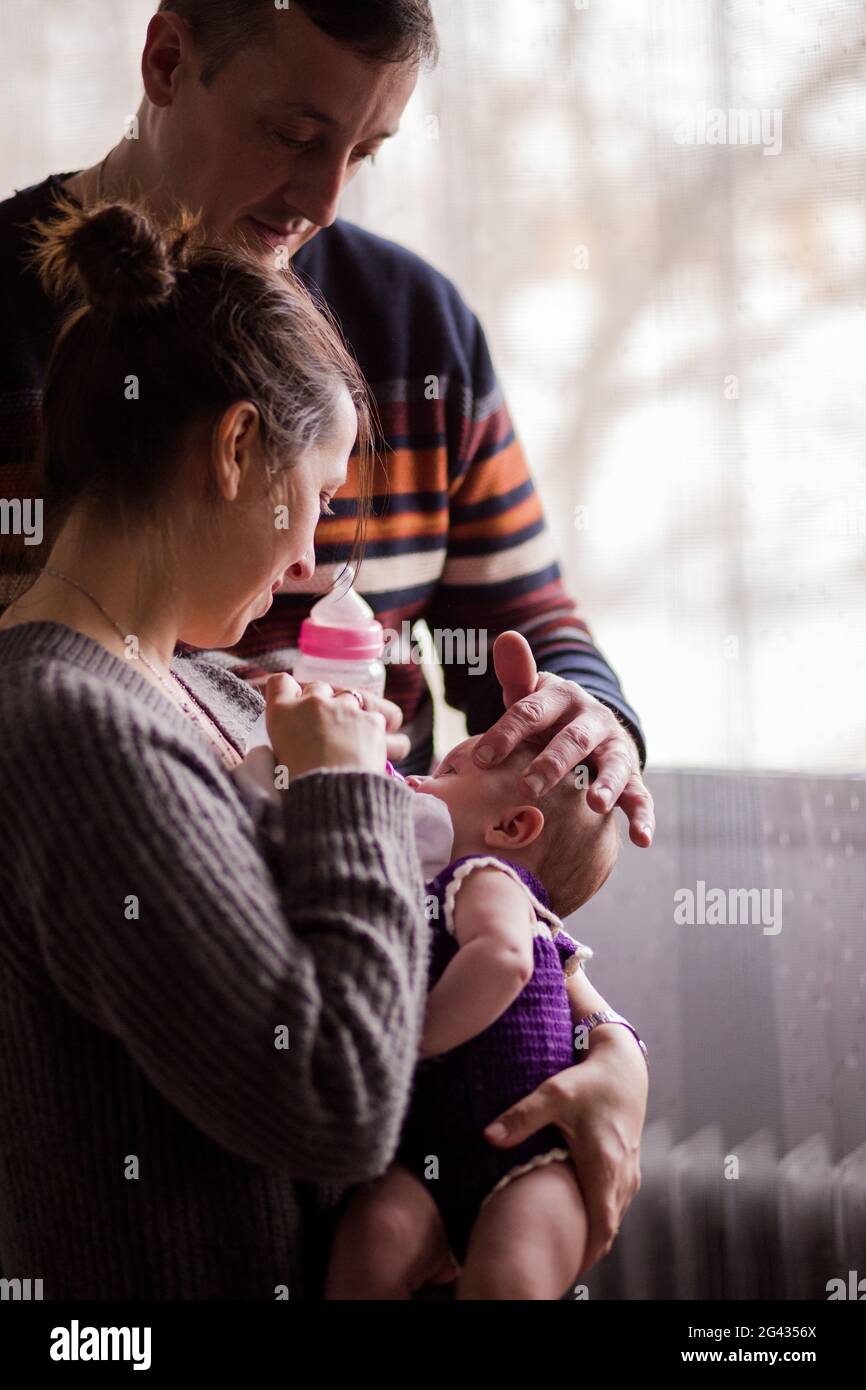 Slav Bulgarian couple with a baby. Father and mother feeding theirs firstborn daughter with a milk bottle. Fathers day and Mothers day Stock Photo