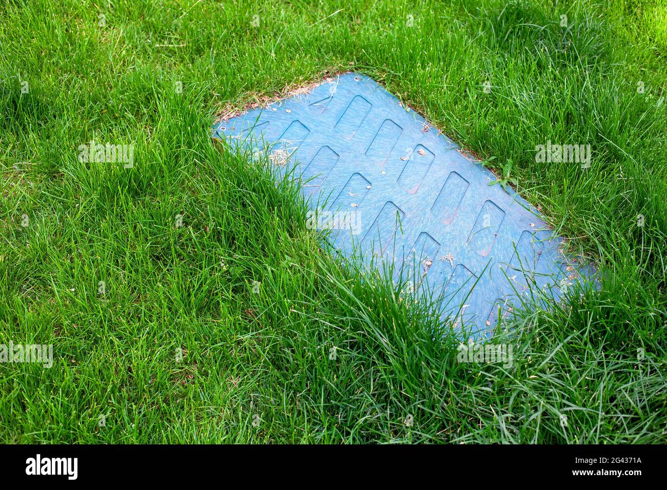 plastic rectangular septic tank manhole cover in green grass on the lawn, engineering systems in outdoor park. Stock Photo