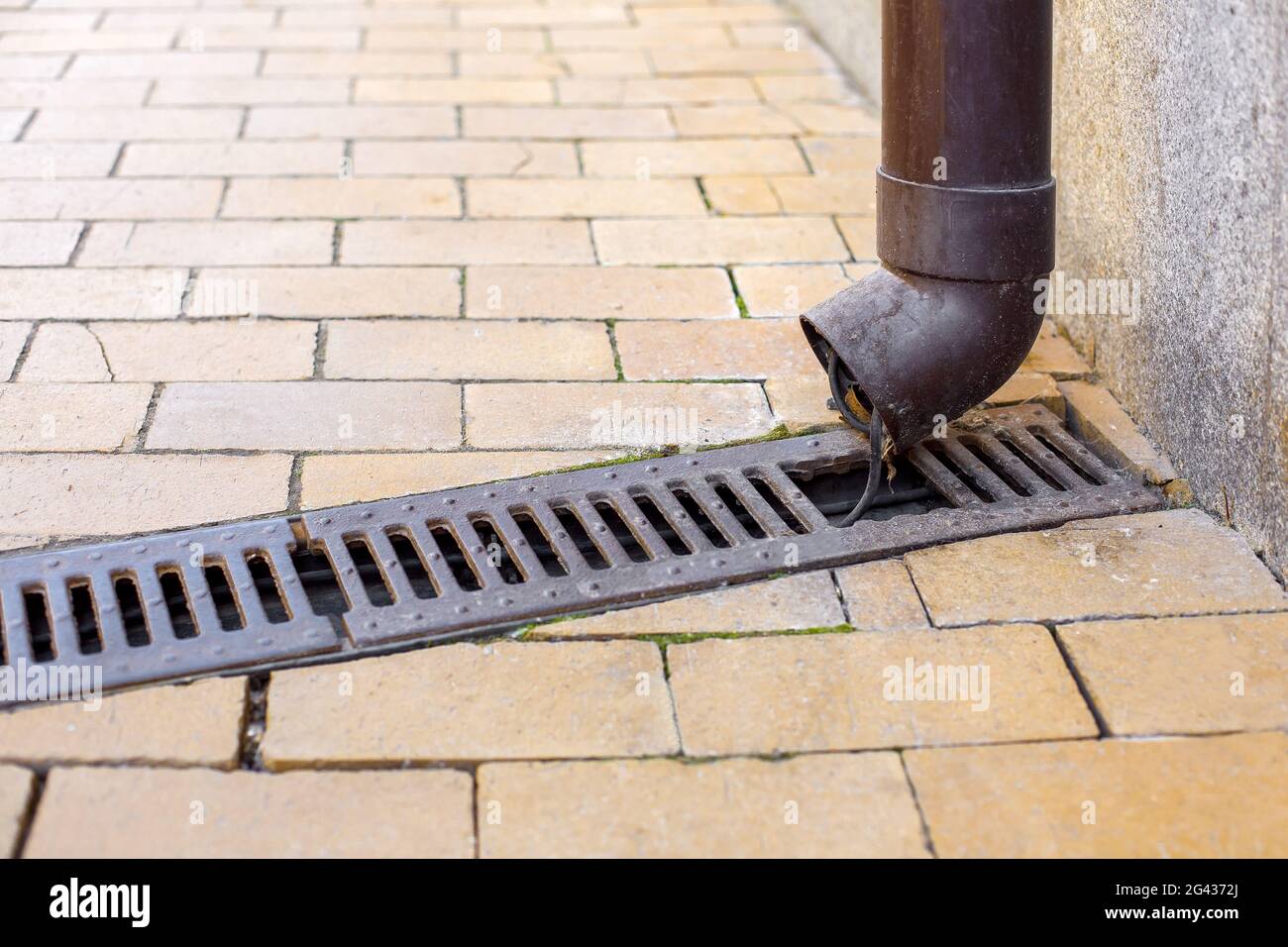 pvc downpipe rainwater system with a drainage grate on a stone tile sidewalk and a house with a pipe close-up of a rainwater drainage system. Stock Photo