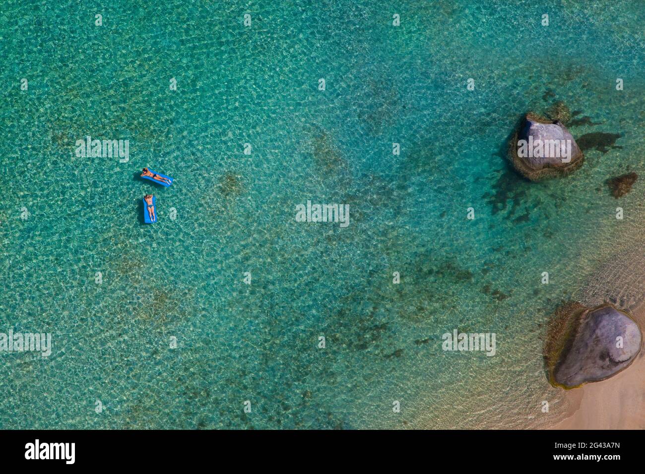Two women, floating on on rubber mattresses on clear, blue water. Shot from the air. British Virgin Islands. Stock Photo